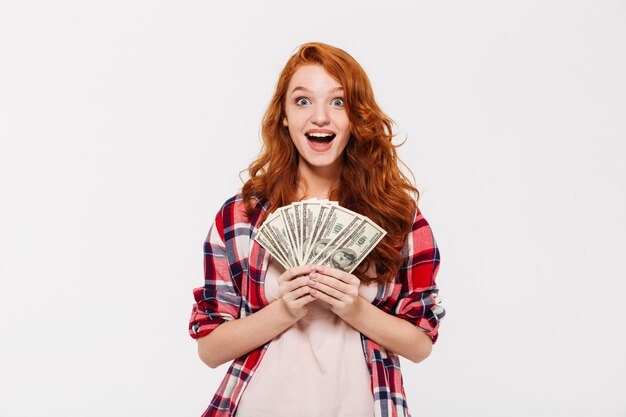 Surprised pretty young redhead lady holding money.