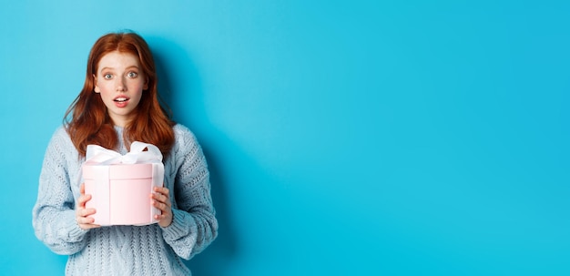 Free photo surprised redhead girl receiving valentines gift holding box with present and staring at camera amaz