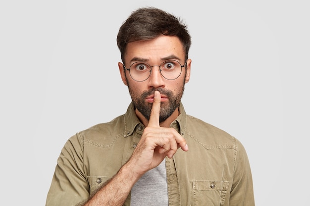 Foto gratuita un uomo europeo con la barba lunga e spaventato sorpreso fa un gesto di silenzio, spera di lealtà e silenzio, chiede di mantenere segrete le informazioni