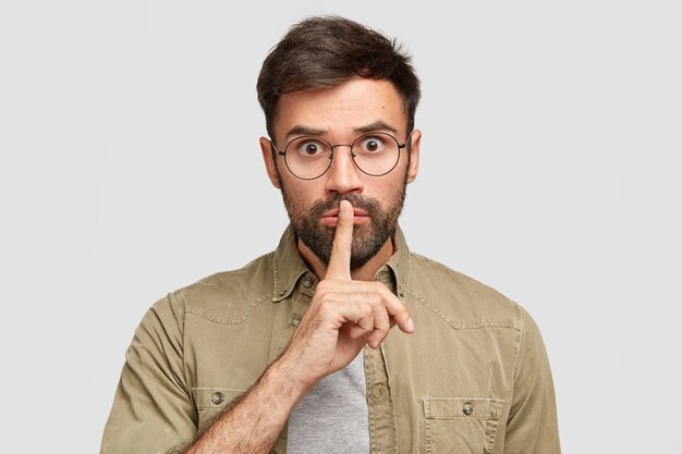 Surprised scared unshaven European man makes hush gesture, hopes for loyalty and silence, asks to keep information in secret
