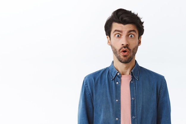 Surprised shocked handsome bearded man with stylish haircut looking shocked stare astonished with dropped jaw gasping from amazement popping eyes impressed standing white background