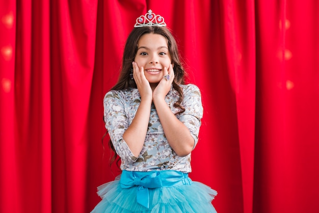 Free photo surprised smiling girl standing in front of red curtain