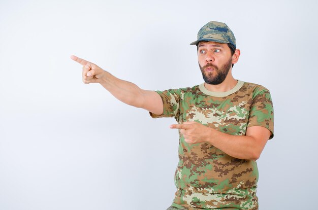 Surprised soldier is pointing away with forefingers on white background