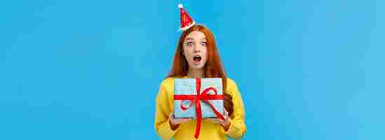 Free photo surprised startled pretty redhead girl receive unexpected gift for christmas classmate open mouth as