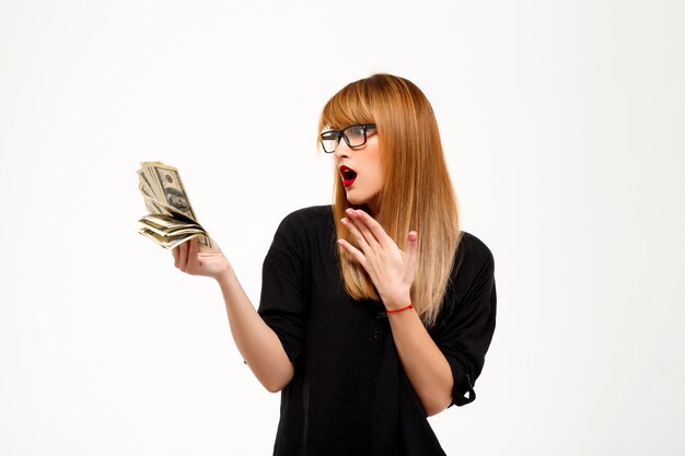 Surprised successful businesswoman holding money over white wall