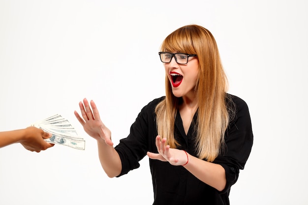 Surprised successful businesswoman reaching for money over white wall