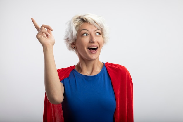 Foto gratuita superwoman sorpresa con mantello rosso rivolto verso l'alto e guardando il lato isolato sul muro bianco