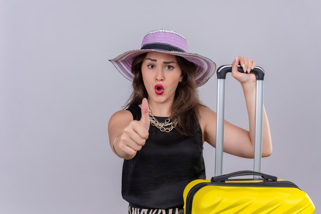 Surprised traveler young girl wearing black undershirt in hat her thumb up on white background