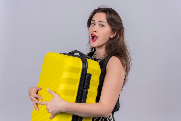 Surprised traveler young girl wearing black undershirt holding suitcase on white background