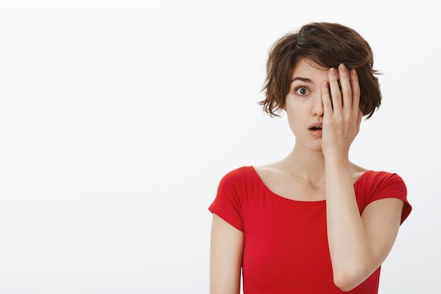 Free photo surprised woman gasping and looking amazed, cover half of face