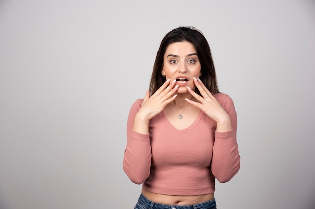 Foto gratuita donna sorpresa che tiene le guance con le mani su un muro grigio.