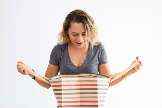 Surprised woman holding shopping bag and peeping into it