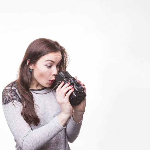 Surprised woman looking in vintage camera over white background