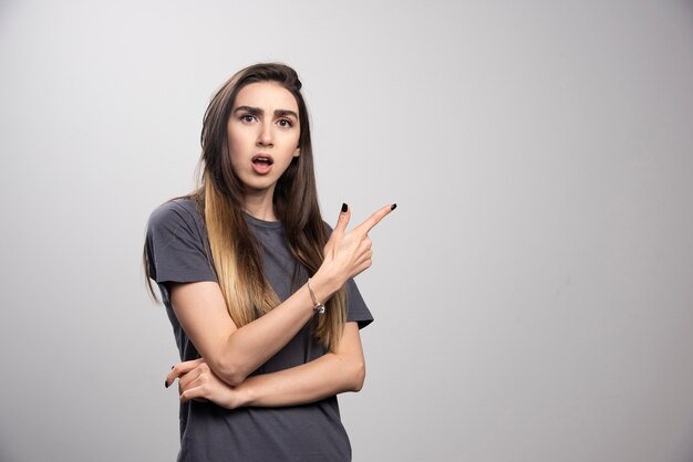 Surprised woman pointing up over a gray background.