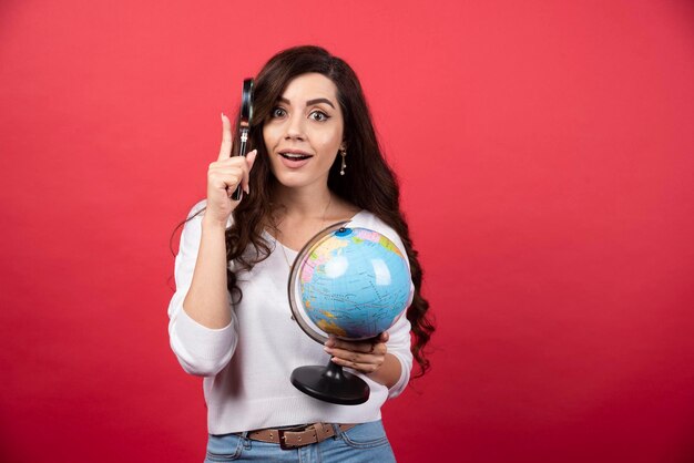 Surprised woman posing with globe and magnifying glass. High quality photo