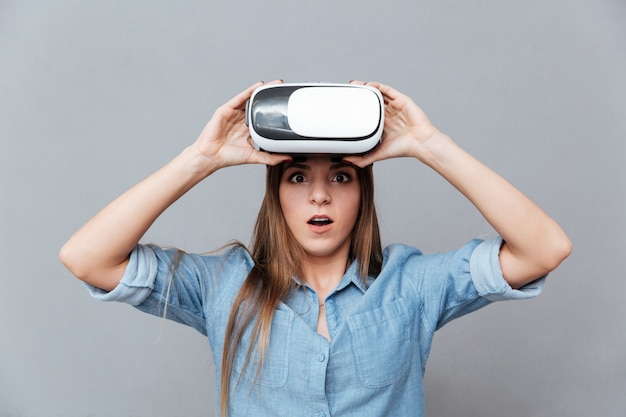 Удивленная женщина в рубашке снимает устройство виртуальной реальности