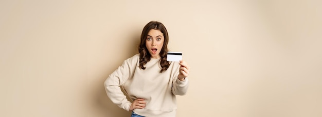 Surprised woman showing credit card gasping impressed impression of discounts or shopping standing o