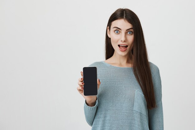 Surprised woman showing smartphone screen amazed