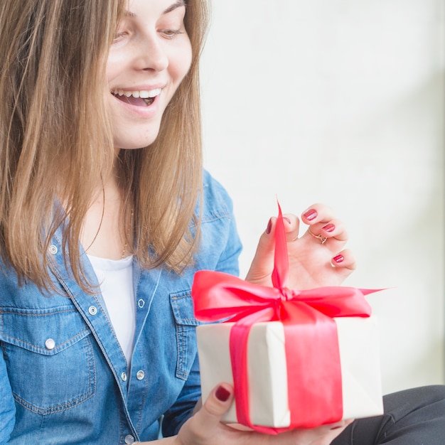 Удивленная женщина, разворачивающая подарочную коробку с подарками