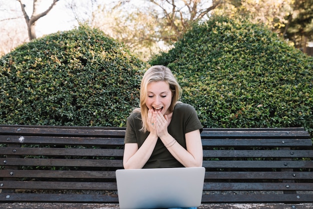 Surprised woman using laptop on bench