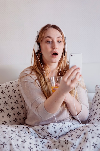 Free photo surprised woman with juice using smartphone