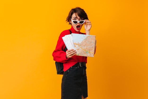 Surprised woman with map touching sunglasses