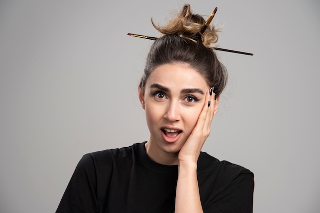 Free photo surprised woman with messy bun standing on gray wall.