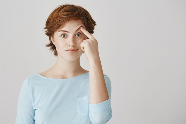 Surprised and wondered redhead girl posing against the white wall