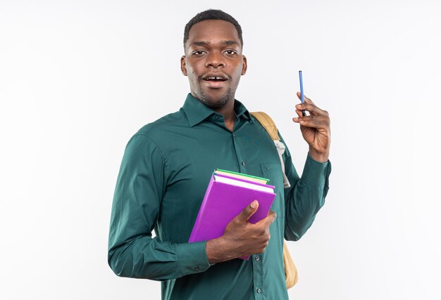 Удивленный молодой афро-американский студент с рюкзаком, держащим книги и ручку