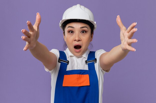 Surprised young asian builder girl with white safety helmet stretching out her hands