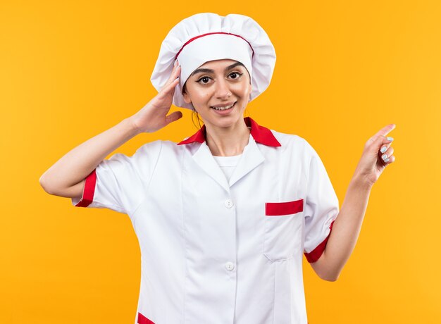 Surprised young beautiful girl in chef uniform points at side 