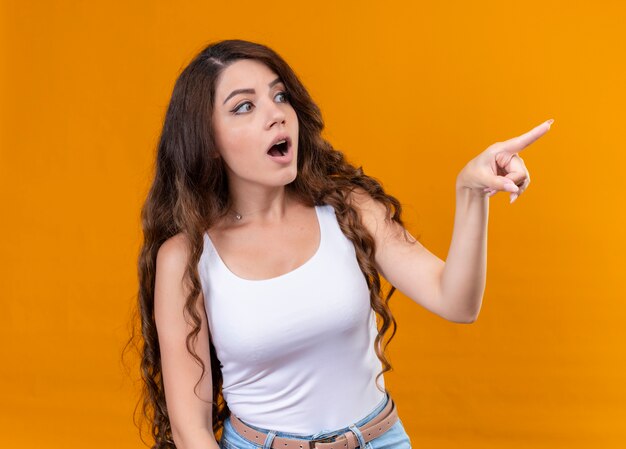 Surprised young beautiful girl pointing at right side on isolated orange wall
