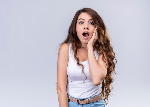 Surprised young beautiful girl putting hand on cheek on isolated white wall with copy space