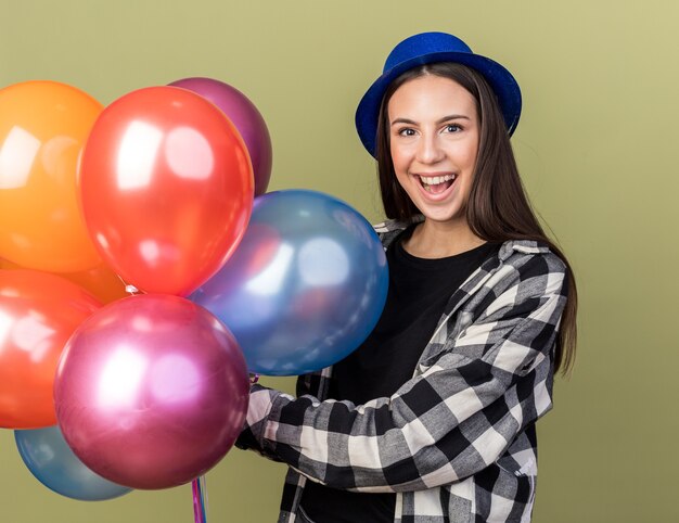 Surprised young beautiful girl wearing blue hat holding balloons 