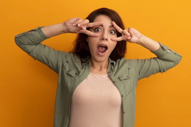 Surprised young beautiful girl wearing olive green t-shirt showing peace gesture isolated on yellow wall