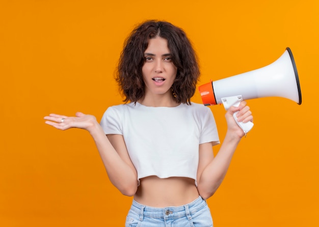 Foto gratuita giovane bella donna sorpresa che tiene altoparlante e che mostra la mano vuota sulla parete arancione isolata