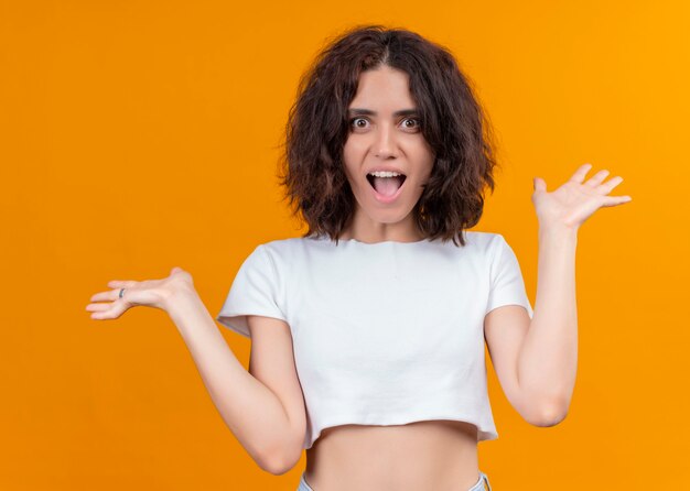 Surprised young beautiful woman with open arms on isolated orange wall