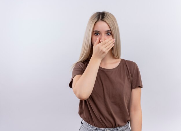 Surprised young blonde girl with hand on mouth on isolated white wall with copy space