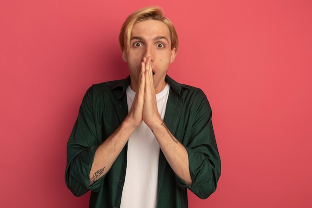 Surprised young blonde guy wearing green t-shirt showing pray gesture