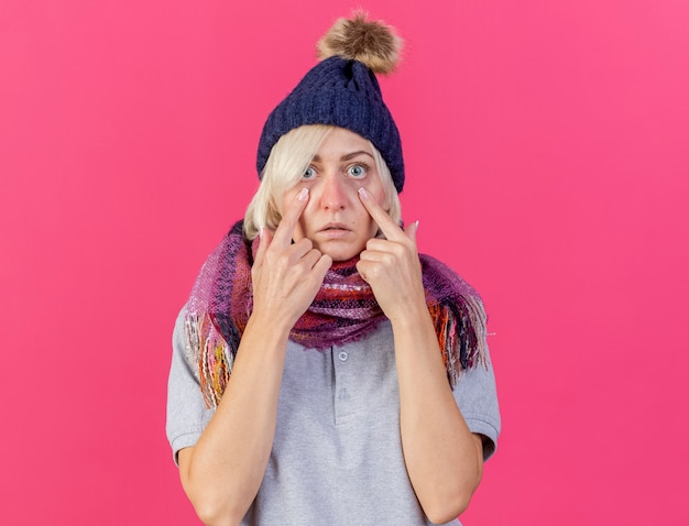 Foto gratuita la giovane donna slava malata bionda sorpresa che indossa il cappello e la sciarpa di inverno abbassa le palpebre isolate sulla parete rosa con lo spazio della copia