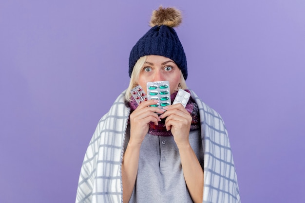 Surprised young blonde ill slavic woman wearing winter hat and scarf