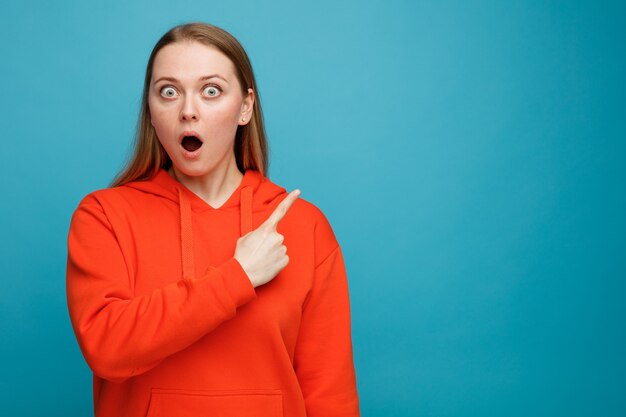 Surprised young blonde woman pointing up at corner 