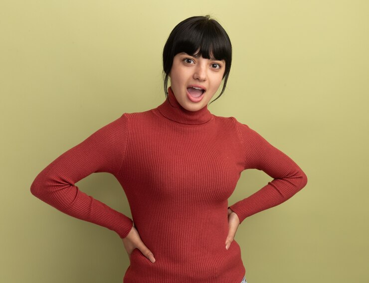 무료 Photo 놀란 된 젊은 갈색 머리 백인 여자 허리에 손을두고 올리브 그린에 카메라를 쳐다 본다