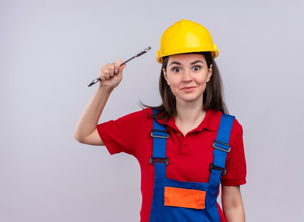 Surprised young builder girl holds workshop key and looks at camera on isolated white background with copy space