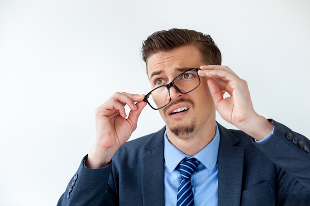 Surprised young businessman putting off glasses