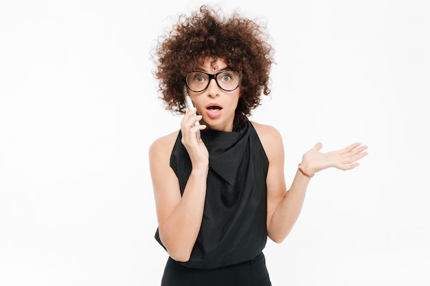 Surprised young businesswoman in eyeglasses talking on mobile phone