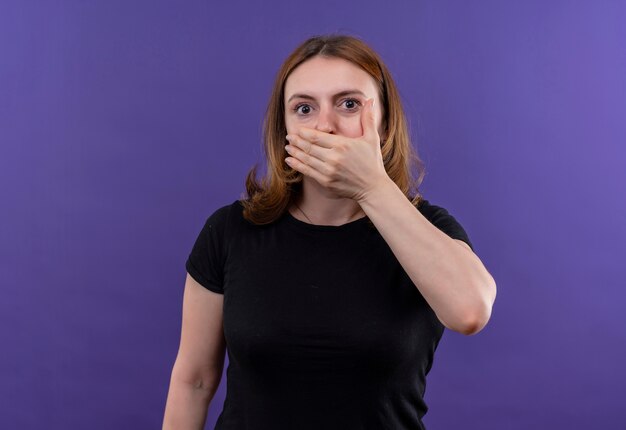 Удивленная молодая повседневная женщина, закрывающая рот рукой на изолированной фиолетовой стене с копией пространства