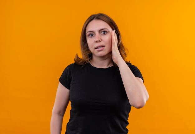 Surprised young casual woman putting hand on cheek on isolated orange wall with copy space