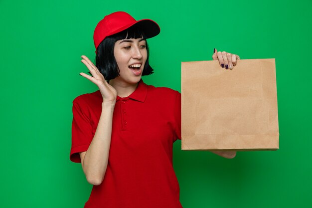 Surprised young caucasian delivery girl holding and looking at paper food packaging
