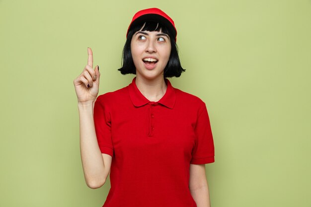 Surprised young caucasian delivery girl pointing up